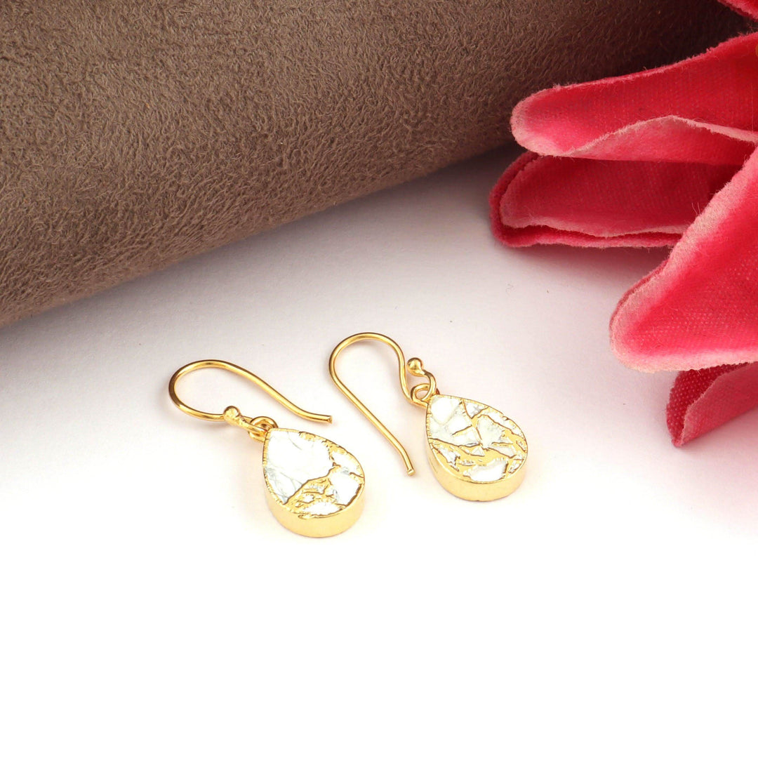 Gold earrings on a white surface with a brown and red fabric background