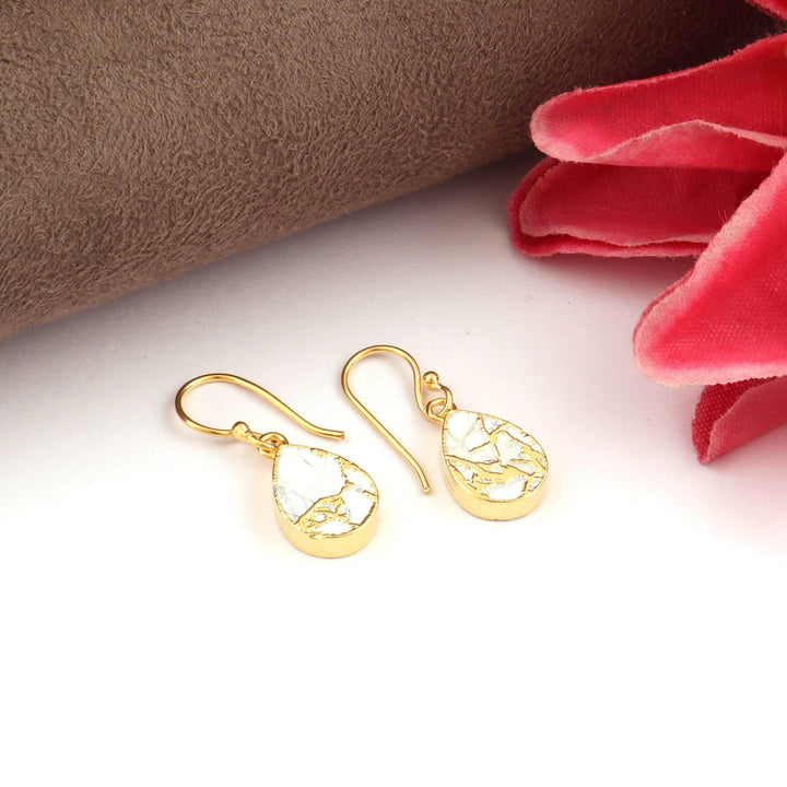 Gold earrings on a white surface with a brown and red fabric background