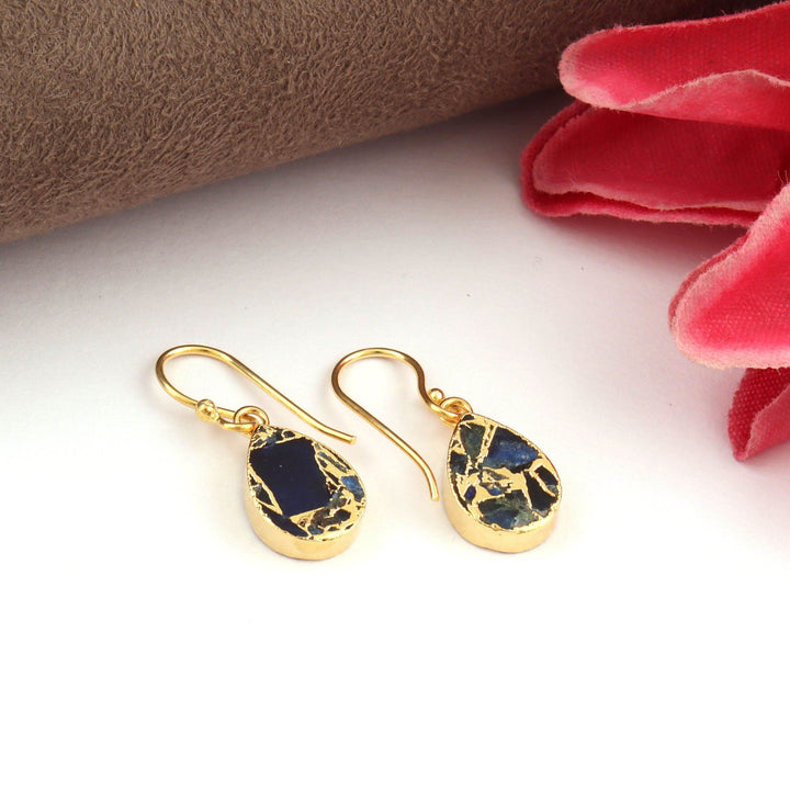Gold earrings with blue stones on a white surface with red fabric in the background