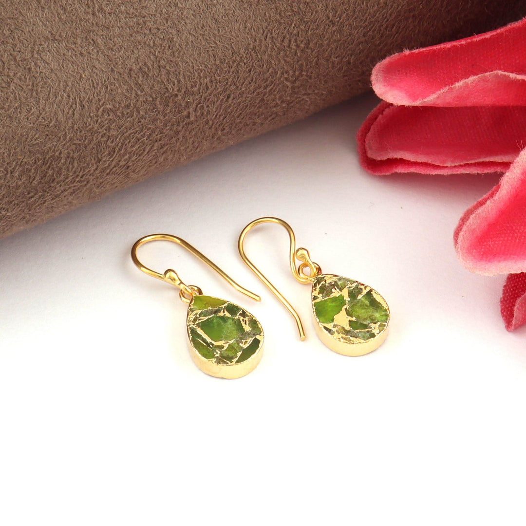 Gold earrings with green gemstones on a white surface with a red fabric