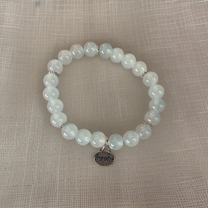 Beaded bracelet with a 'Inspire' charm on a textured beige background