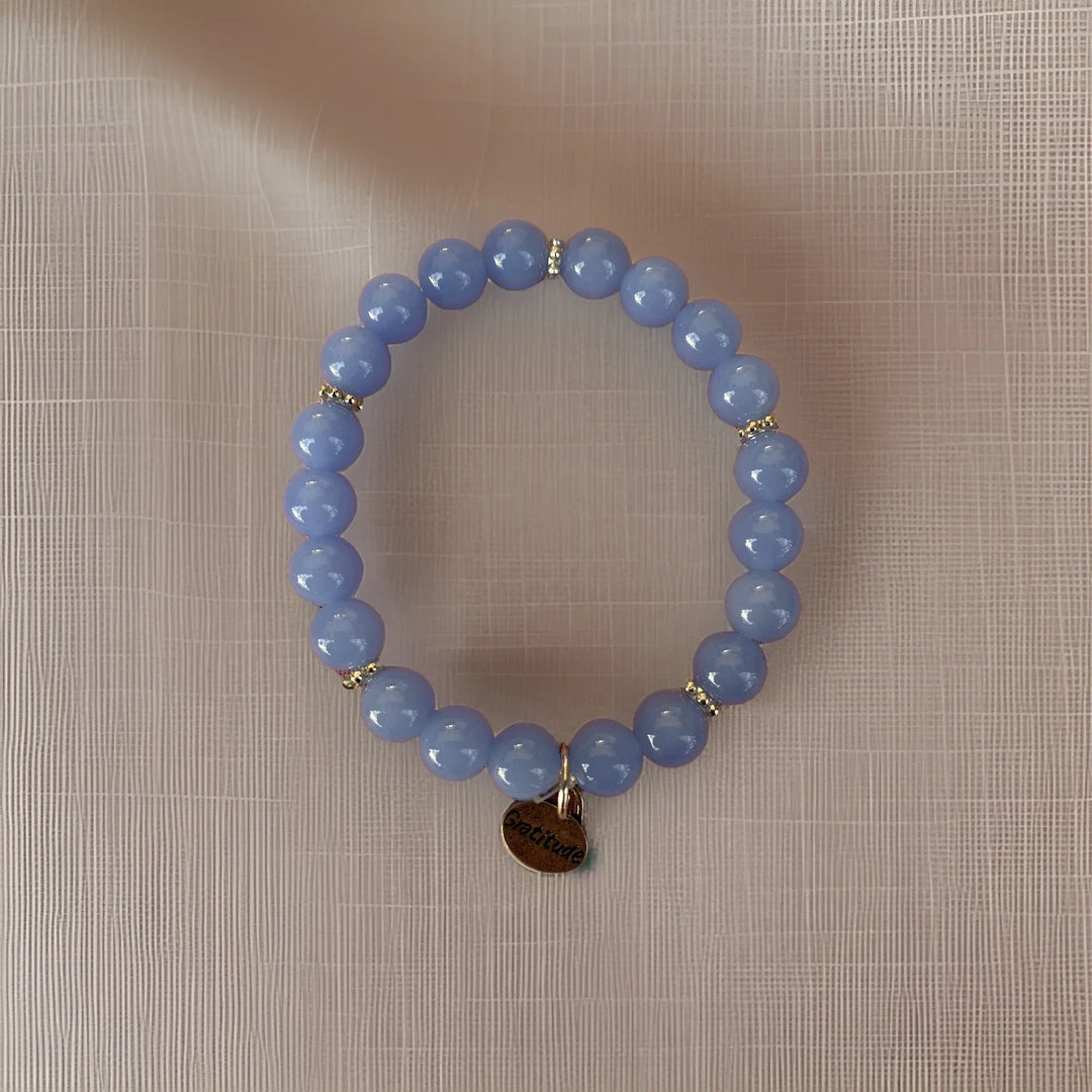 Blue beaded bracelet with a gold tag on a beige textured background