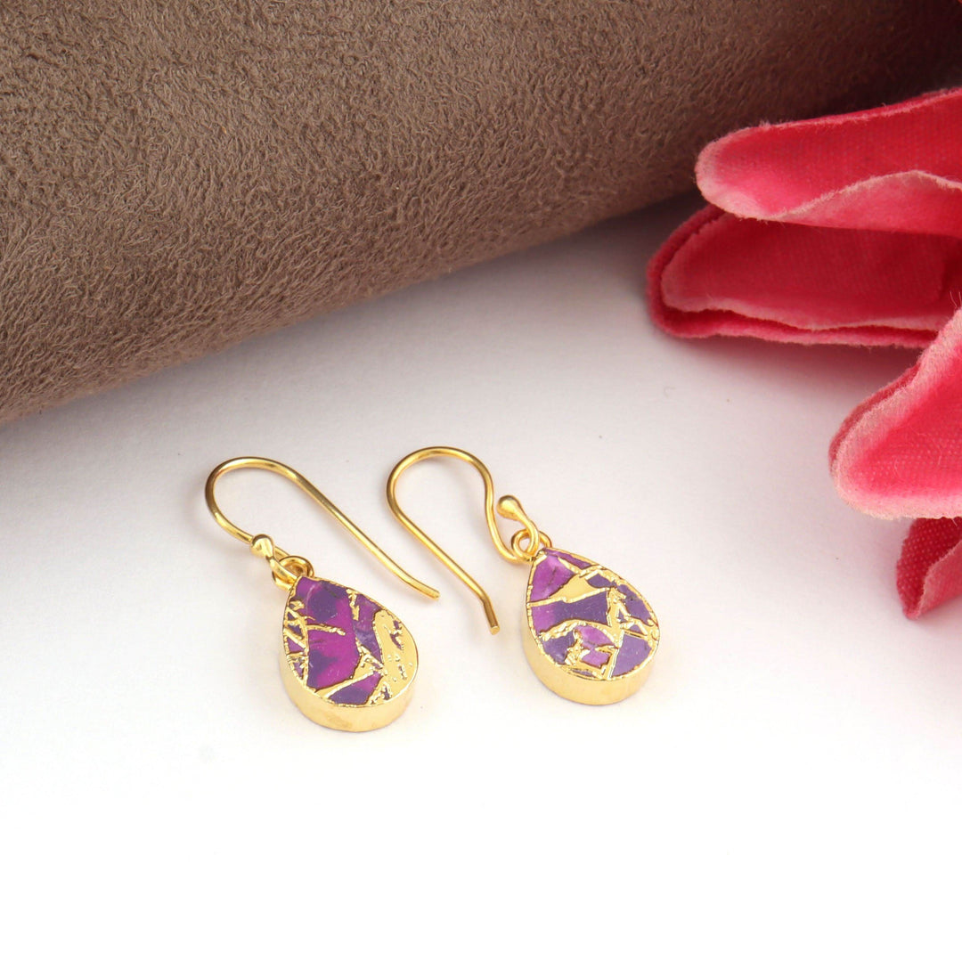 Gold earrings with purple stone on a white surface with pink fabric