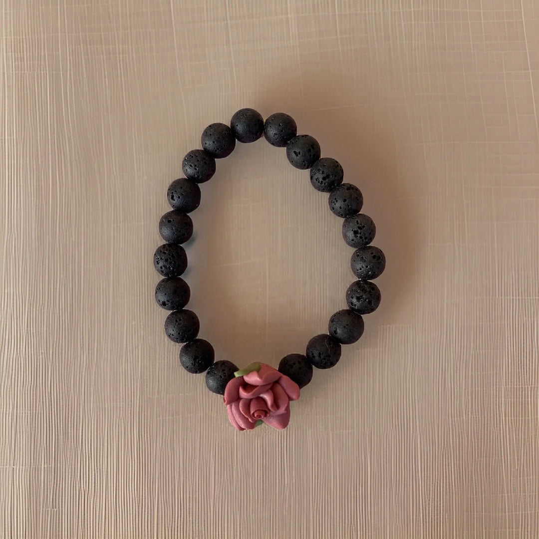 Black beaded bracelet with a pink rose charm on a beige surface