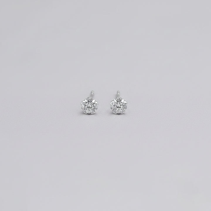 A close-up of a hand displaying a pair of small silver stud earrings with clear round-cut stones.
