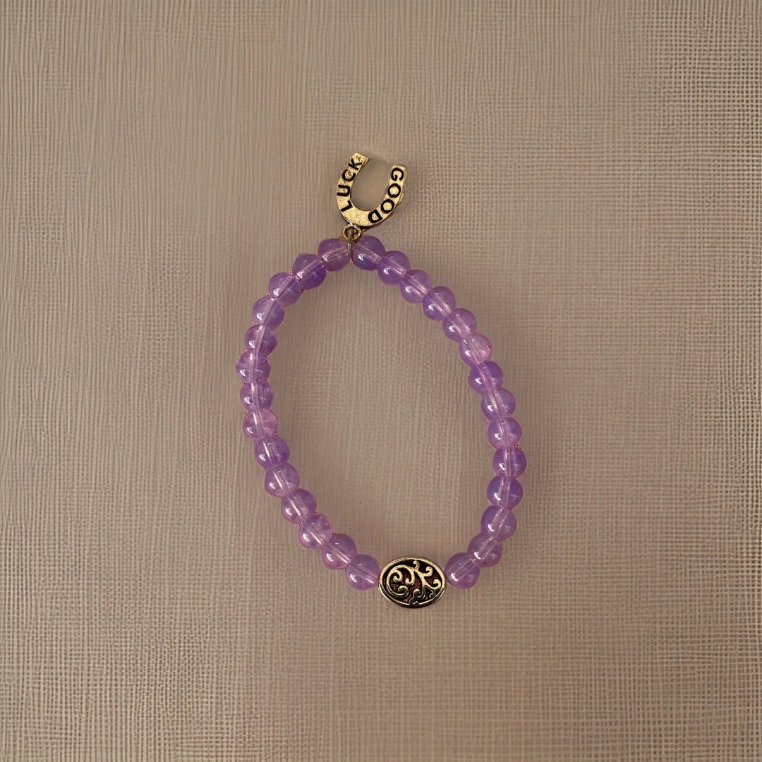 Purple beaded bracelet with gold charms on a beige background