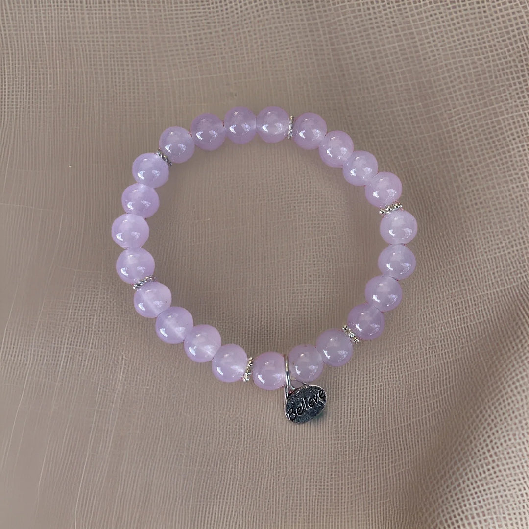 Purple beaded bracelet with a silver tag on a beige fabric background