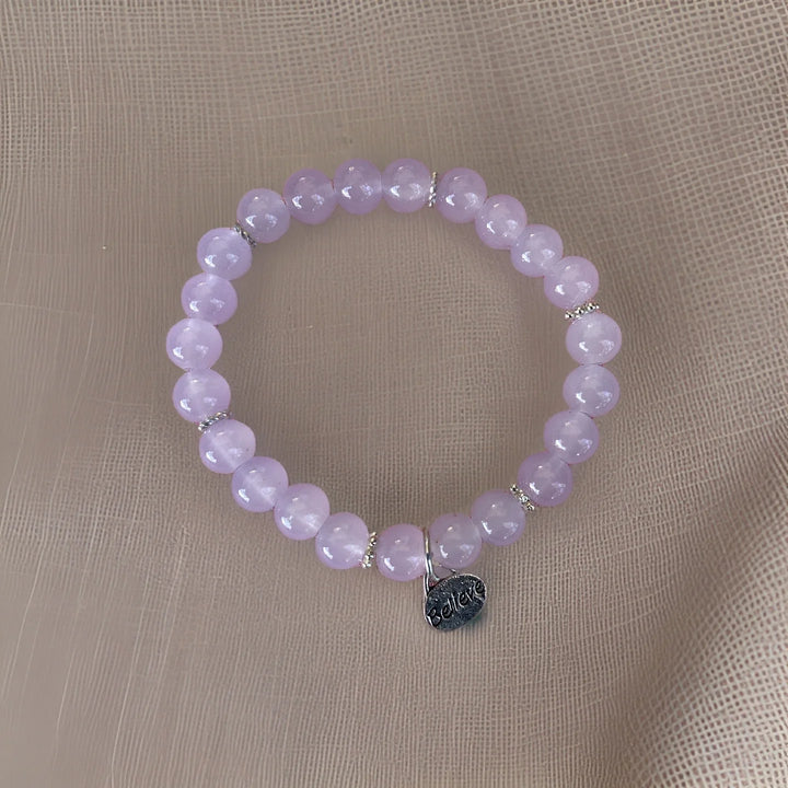 Purple beaded bracelet with a silver tag on a beige fabric background