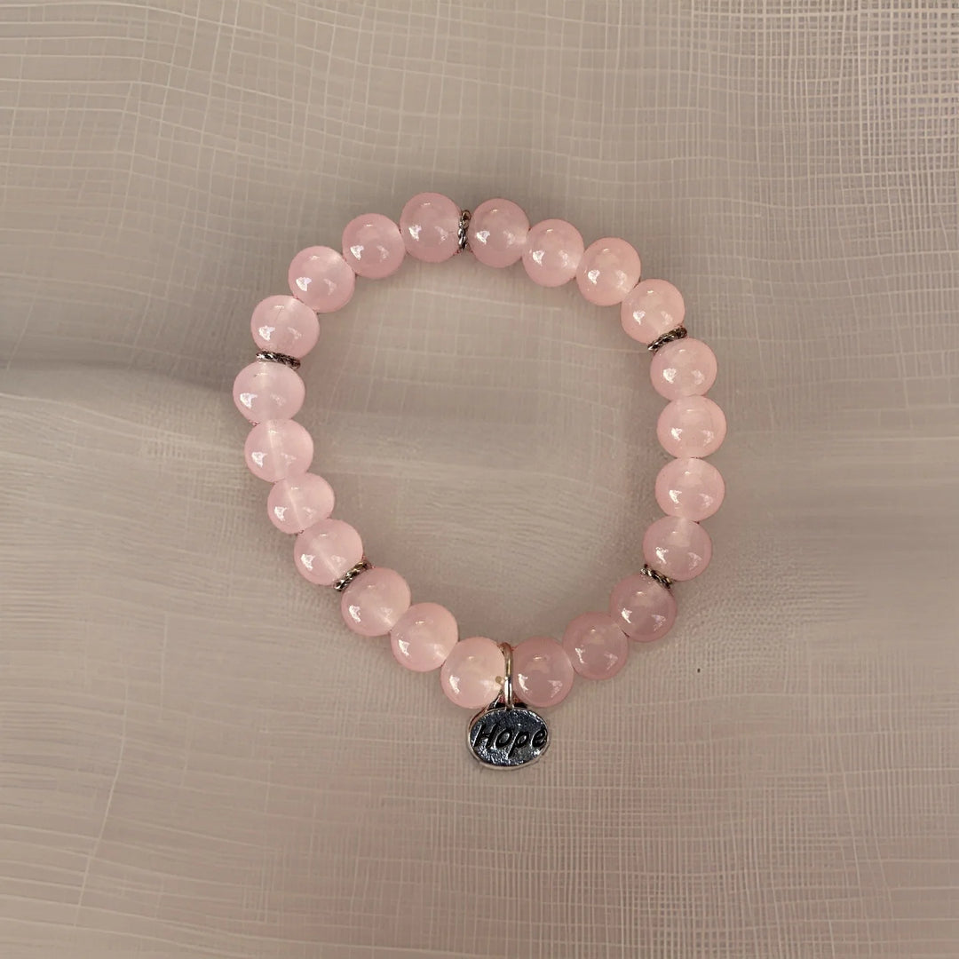 Pink beaded bracelet with a 'Hope' charm on a beige fabric background